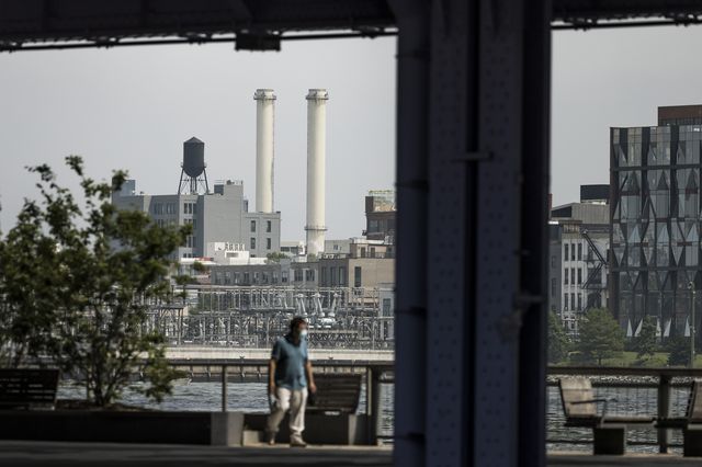 People in a park along the Hudson River with a view of smoke stacks in the background.